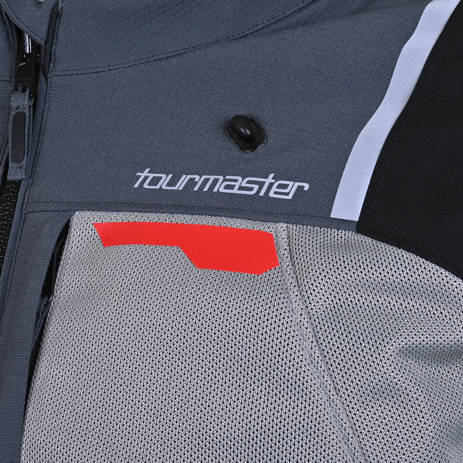 Primer plano técnico de chaqueta de moto Tourmaster gris oscura con logo blanco, cremallera negra, paneles de malla, detalles reflectantes blancos y naranjas.