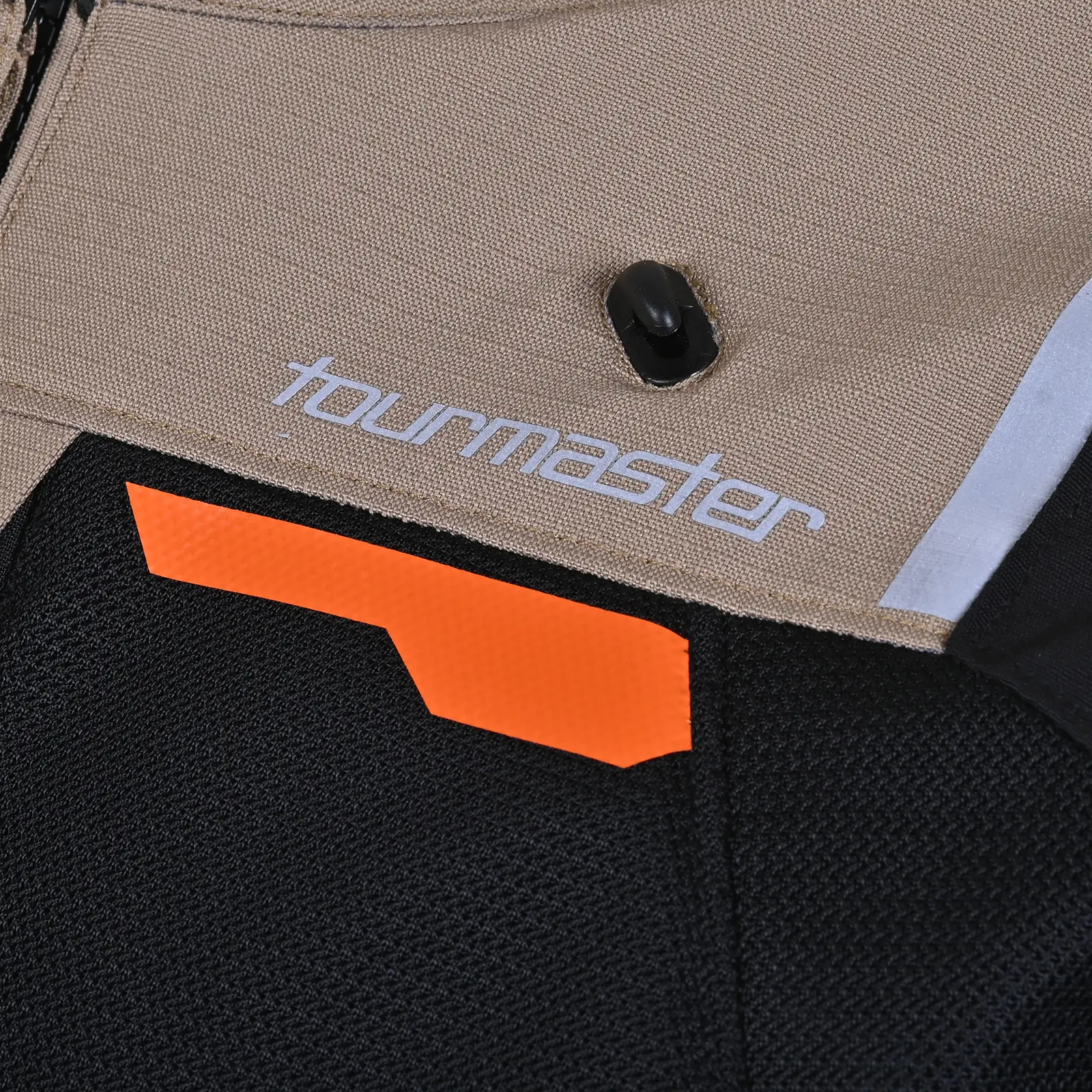 Primer plano de tejido de chaqueta Tourmaster beige y negro con logo, franja naranja y detalle reflectante.