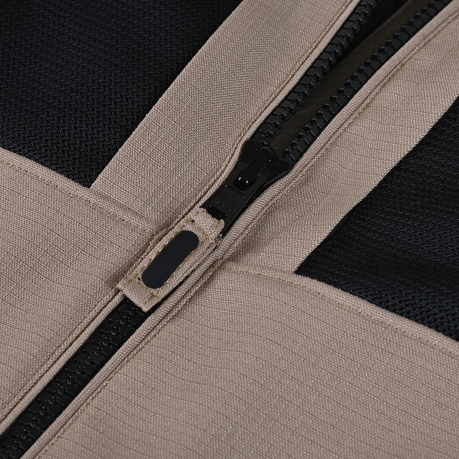 Primer plano de un cierre de cremallera negro sobre tela texturizada color beige, con detalles de tejido negro en el fondo.